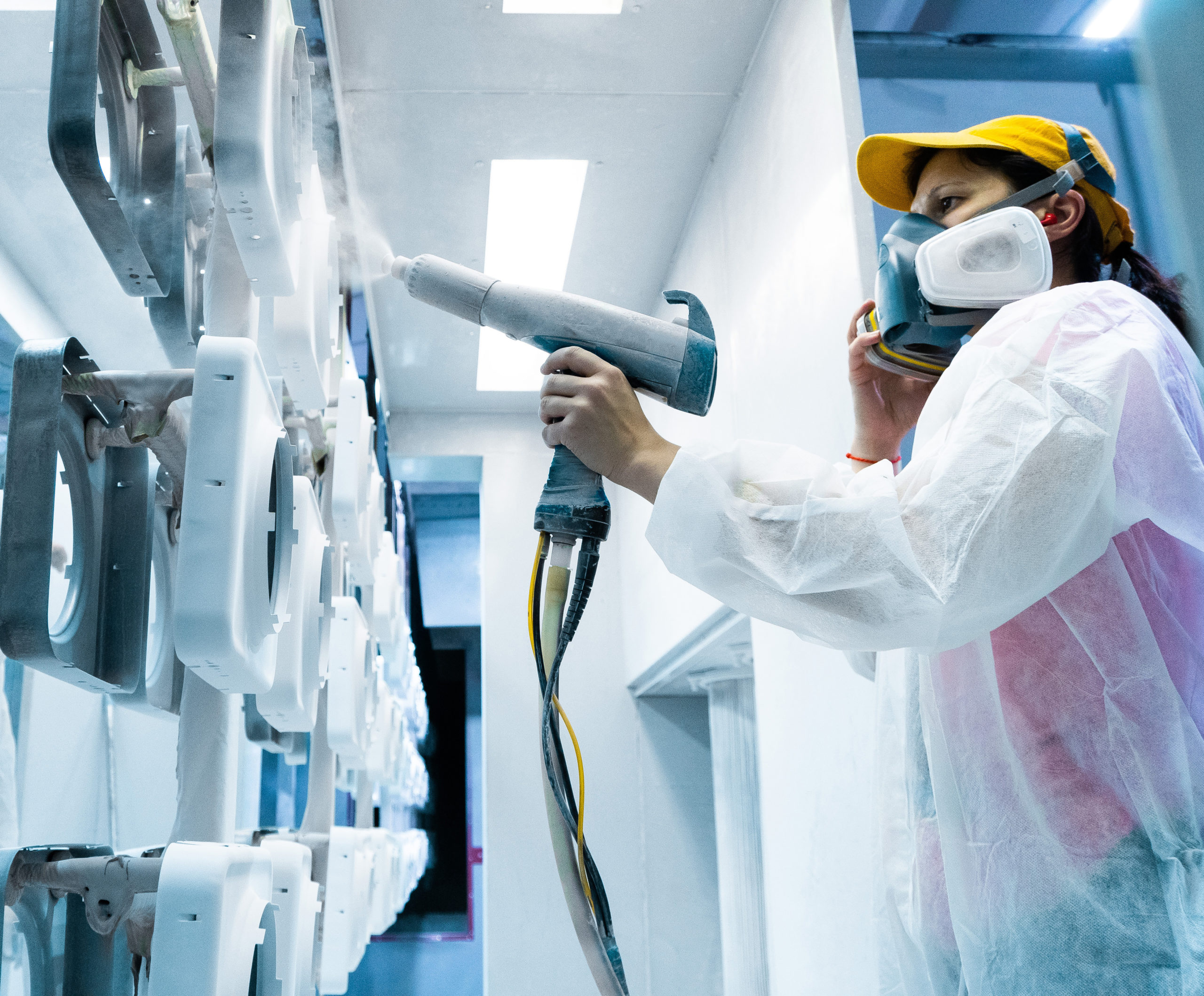 Powder coating of metal parts. A woman in a protective suit sprays white powder paint from a gun on metal products